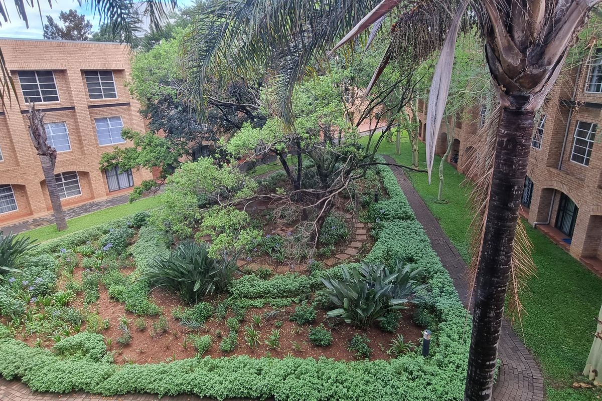 An elevated view of a well-maintained communal garden area surrounded by brick apartment buildings with paved walkways and mature landscaping.