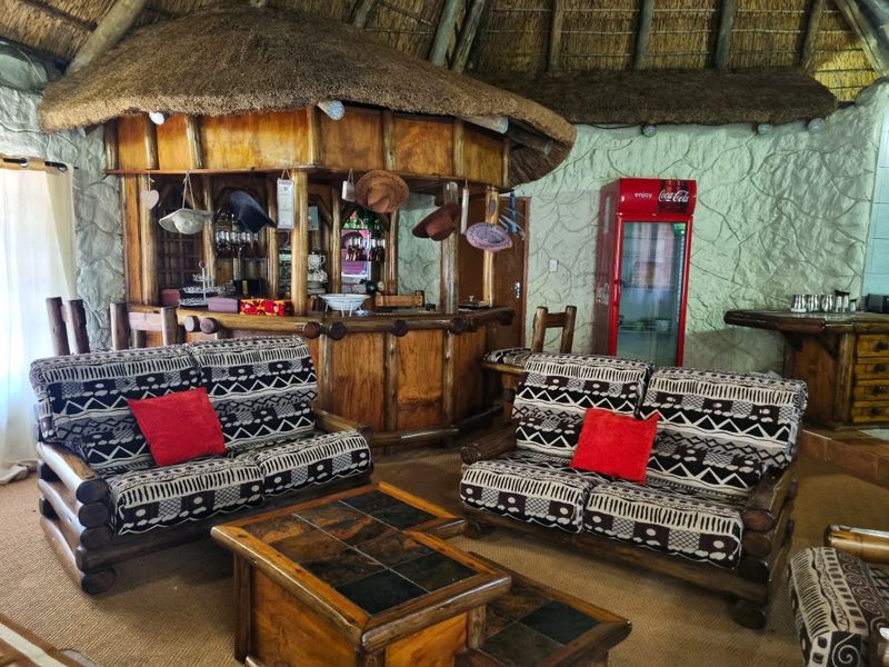 A rustic entertainment area featuring a built-in timber bar, thatched roof ceiling, and textured stone wall finishes.