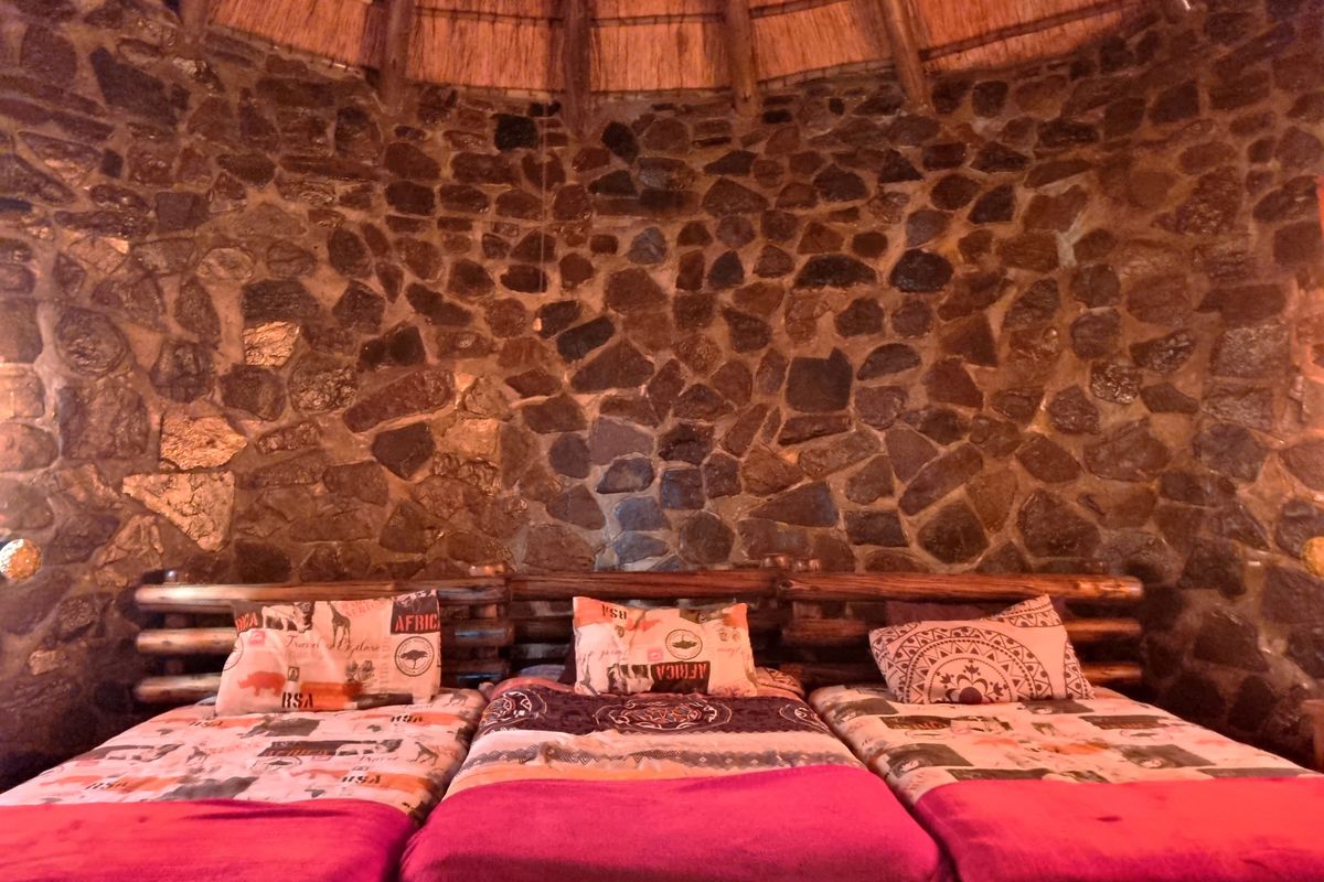 A unique bedroom featuring a rustic exposed stone wall and a traditional thatched roof ceiling.