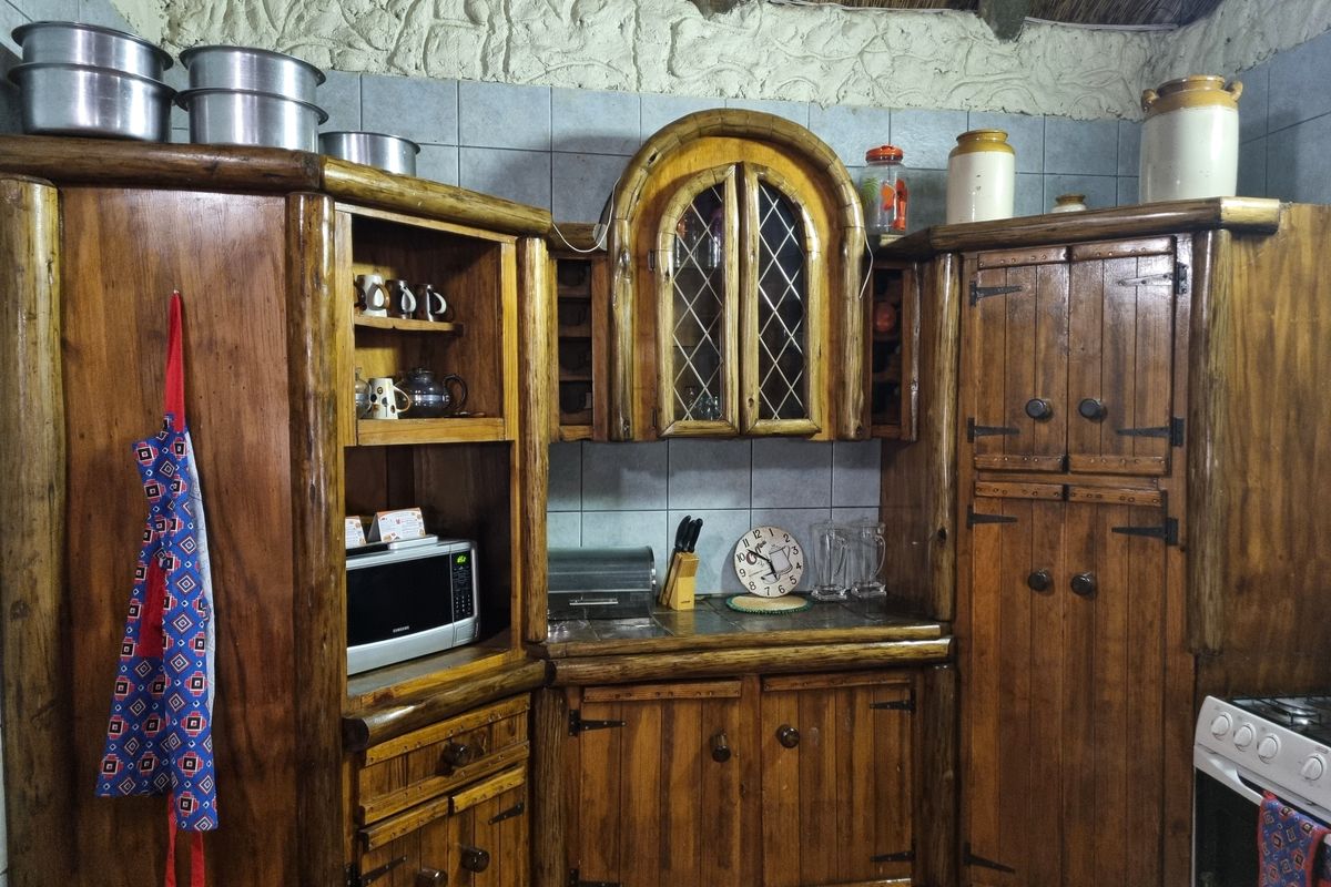 Rustic kitchen featuring custom timber cabinetry, leaded glass detailing, tiled backsplash, and a traditional thatch roof with exposed timber beams.