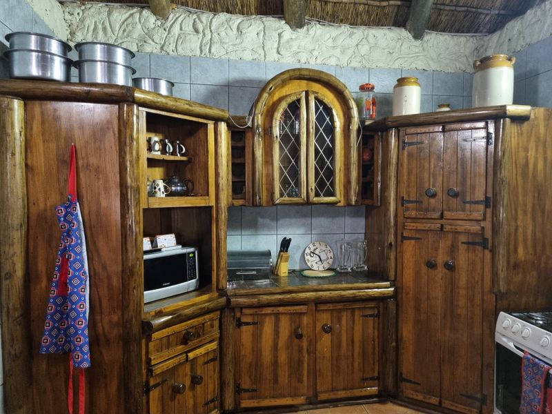 Rustic kitchen featuring custom timber cabinetry, leaded glass detailing, tiled backsplash, and a traditional thatch roof with exposed timber beams.