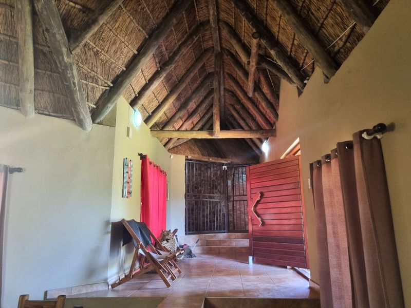 Living area featuring a high vaulted thatched roof with exposed timber trusses, tiled flooring, and a secure entrance with a timber door.