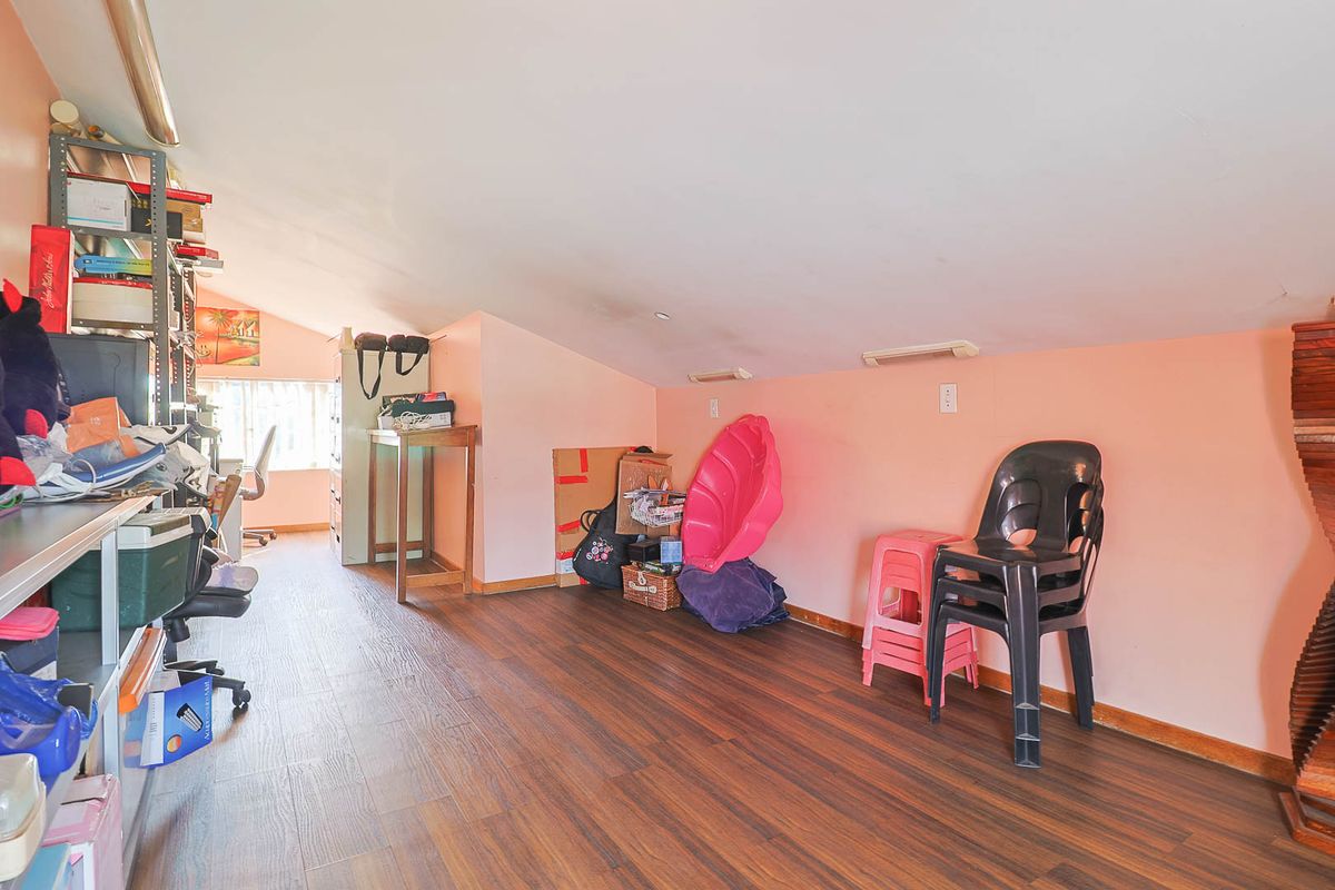 An attic-style bedroom featuring sloped ceilings, laminate flooring, and recessed lighting, currently used as a multi-purpose storage and workspace area.