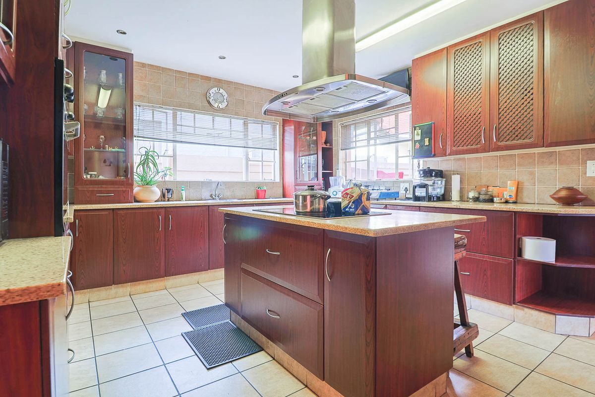 A functional kitchen featuring dark wood cabinetry, a central island with a built-in hob, stainless steel extractor fan, and tiled splashbacks.