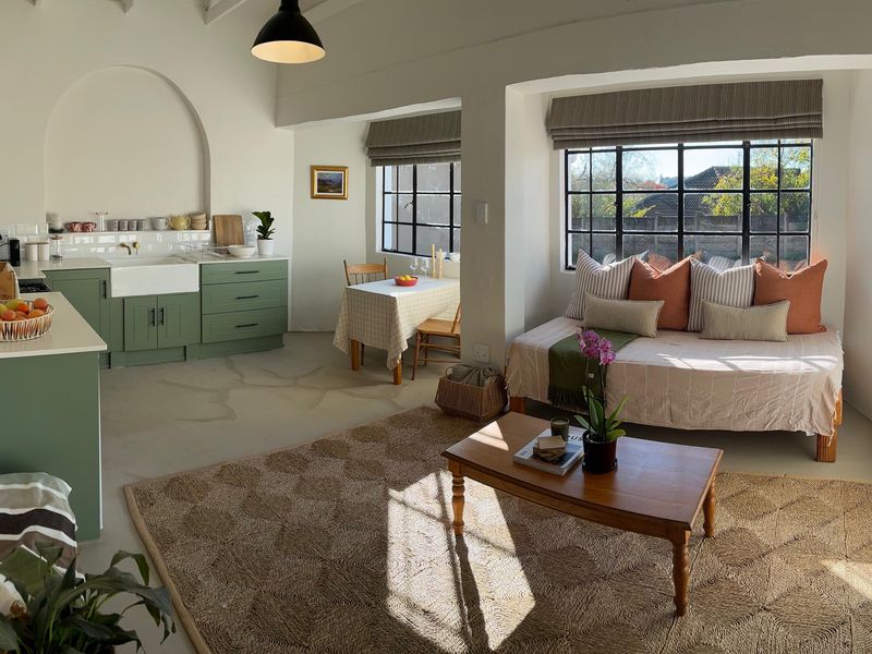 Bright open-plan living area featuring a modern kitchen with green cabinetry, farmhouse sink, and polished concrete floors, seamlessly integrated with a cozy lounge space.