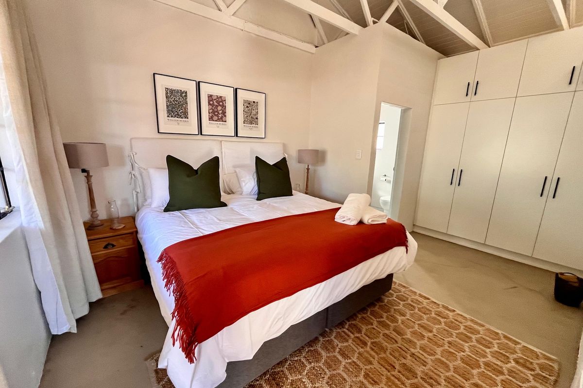 A well-maintained bedroom featuring exposed roof trusses, ample built-in cupboard storage, and direct access to an en-suite bathroom.