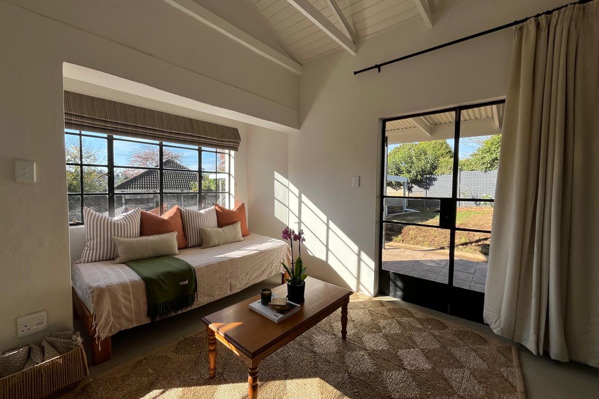 Bright living room featuring vaulted ceilings with exposed rafters, steel-framed windows, and direct access to the rear garden through a glass-paned door.