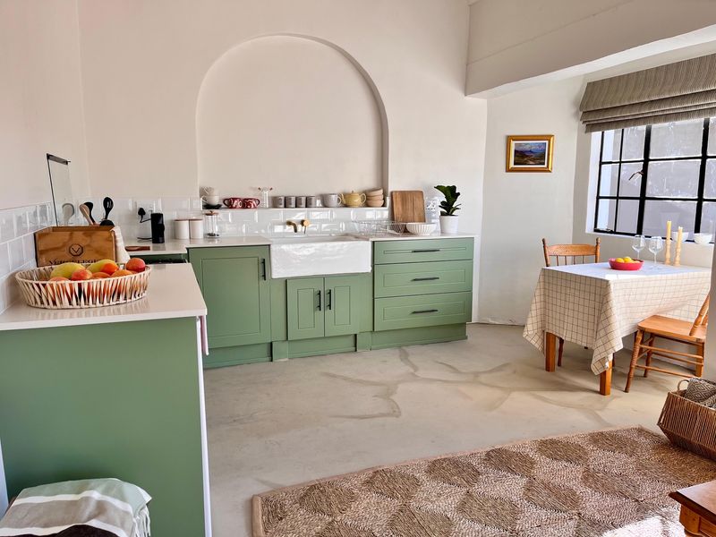 A charming kitchen featuring sage green cabinetry, a classic farmhouse sink, subway tile backsplash, and an elegant arched wall niche, complemented by concrete flooring.