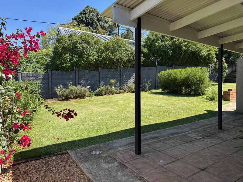 A covered patio area overlooking a private garden with a lawn, established shrubs, and a secure brick boundary wall.