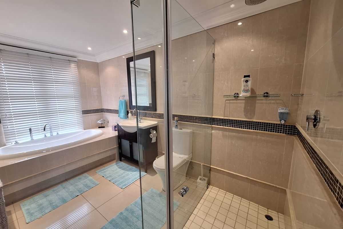 Modern bathroom featuring a tiled walk-in shower with glass enclosure, a built-in bathtub, vanity basin, and toilet with neutral wall and floor tiling.