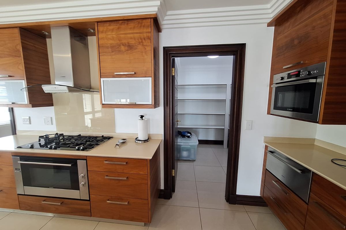 Modern kitchen featuring wood-veneer cabinetry, stone countertops, built-in gas hob, extractor fan, and integrated oven, with an adjacent walk-in pantry or scullery area.