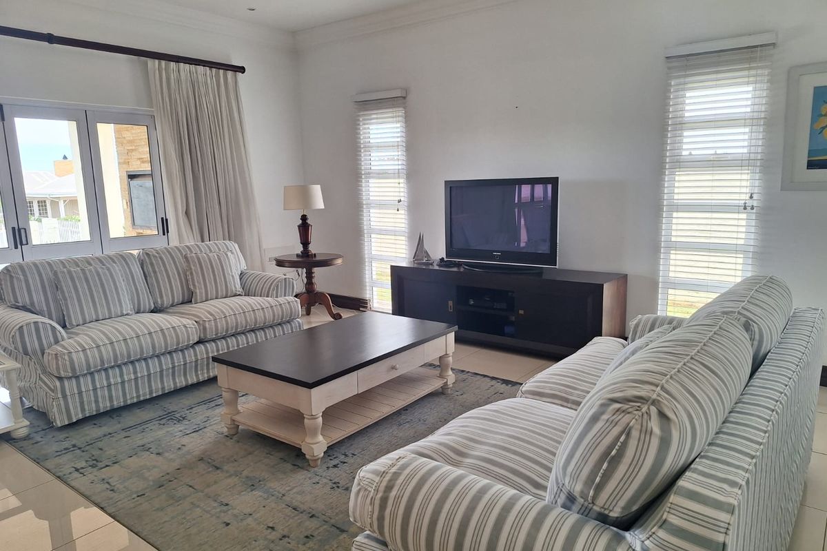 A bright and spacious living room featuring tiled flooring, large windows with fitted blinds, and double doors leading to an outdoor area.