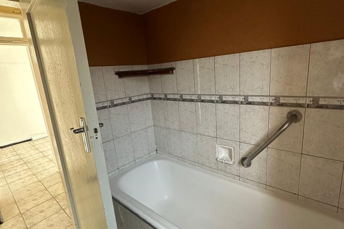 A dated bathroom featuring a built-in bathtub with a grab rail and tiled finishes, requiring cosmetic updates and maintenance.