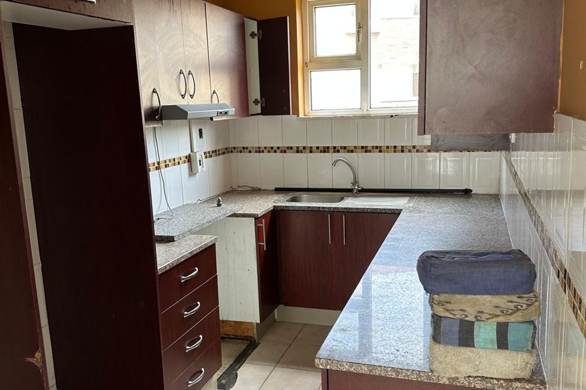 A dated kitchen featuring dark laminate cabinetry, granite-look countertops, a stainless steel sink, and tiled backsplash, requiring cosmetic updates and repairs.