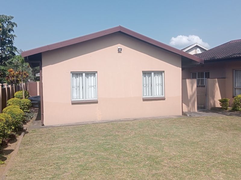 Rear view of the cottage featuring a well-maintained lawn, perimeter wall, and tiled roof structure with security-fitted windows.