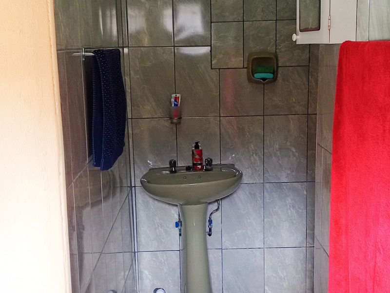 A compact bathroom featuring a pedestal basin, fully tiled walls, and floor, with a wall-mounted medicine cabinet and visible plumbing fixtures.