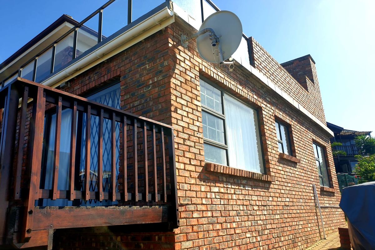 Exterior view of a face brick apartment building featuring a wooden balcony, glass balustrade, and aluminium window frames.