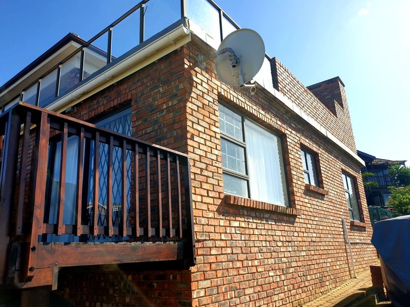 Exterior view of a face brick apartment building featuring a wooden balcony, glass balustrade, and aluminium window frames.