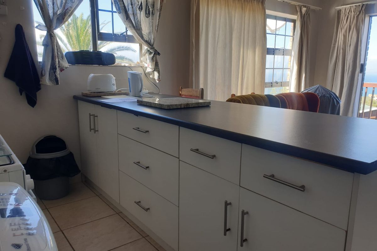 A functional kitchen area featuring white built-in cabinetry, dark laminate countertops, and tiled flooring, with natural light provided by multiple windows.