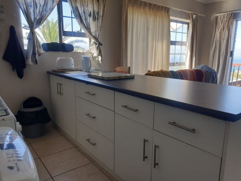 A functional kitchen area featuring white built-in cabinetry, dark laminate countertops, and tiled flooring, with natural light provided by multiple windows.