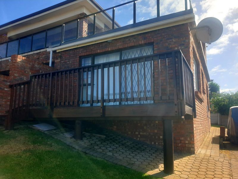 Rear exterior view of the apartment featuring a raised timber deck with balustrade, brick facade, and paved patio area.