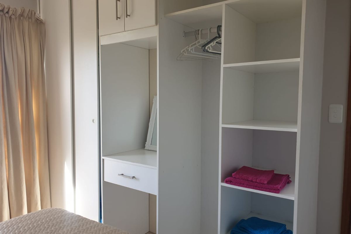 A bedroom featuring a white built-in wardrobe with integrated shelving, hanging space, and a vanity area.