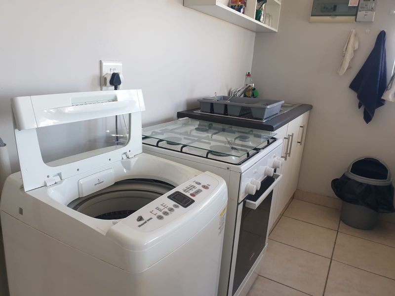 A functional kitchen area featuring a gas stove, oven, built-in cabinetry, and a sink, with tiled flooring throughout.