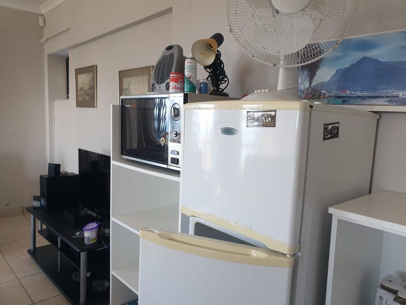 A living area featuring tiled flooring and coving, currently utilized with various household appliances and storage units.