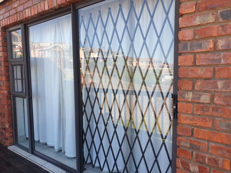 A balcony area featuring a sliding glass door with an integrated expandable security gate, set against an exposed brick exterior wall.