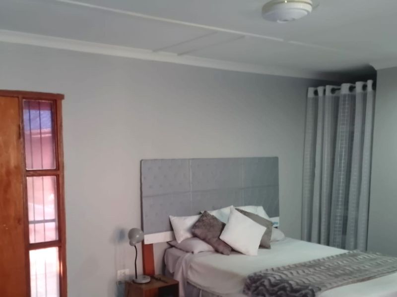 A bedroom featuring neutral wall tones, a built-in cupboard with wooden frame, and window curtains.