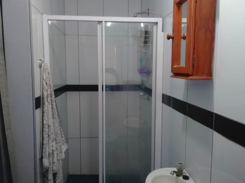 A functional bathroom featuring a shower enclosure with sliding doors, a pedestal basin, and wall-mounted storage cabinetry with tiled walls.