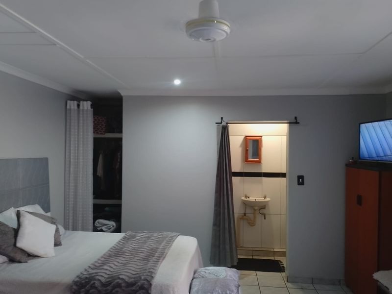 A bedroom featuring a ceiling fan, built-in wardrobe, and an open-plan en-suite bathroom with a wall-mounted basin.