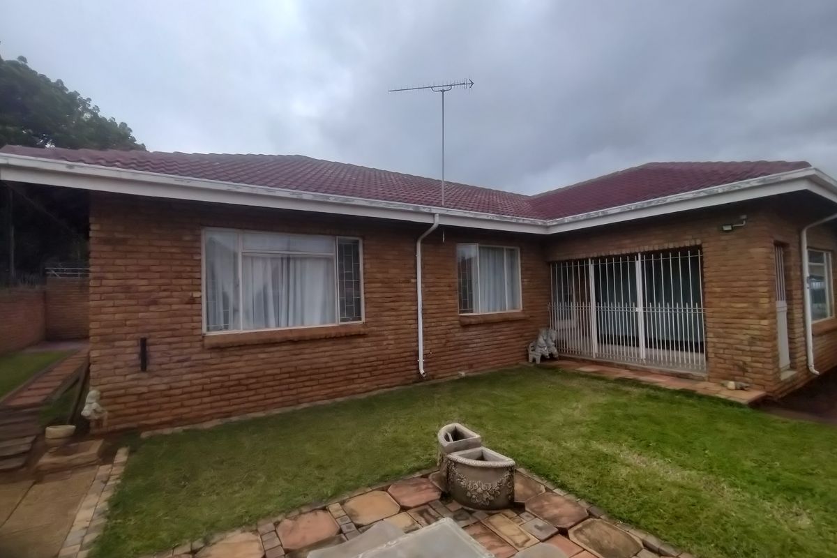 Rear view of a single-story brick house featuring a tiled roof, security bars on windows, and a paved patio area.