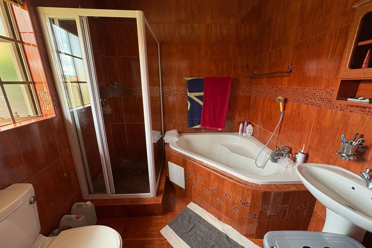 A bathroom featuring a corner bathtub, separate shower enclosure, pedestal sink, and toilet, finished with full-height brown wall tiles.
