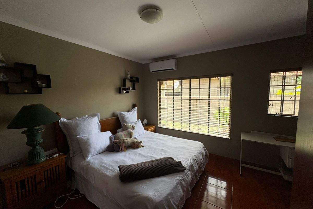 A bedroom featuring tiled flooring, an air conditioning unit, and windows fitted with security bars.