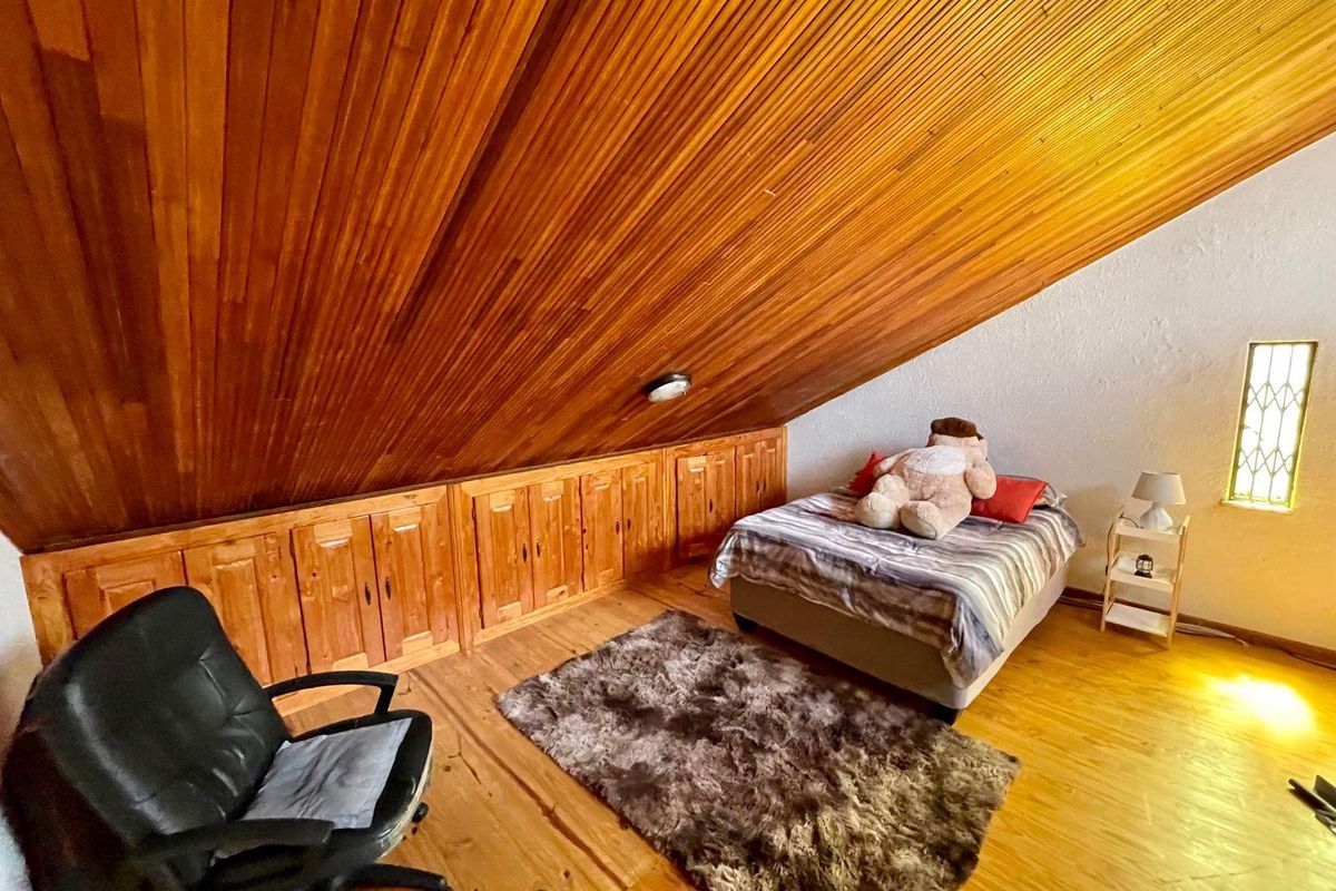 Attic bedroom featuring a sloped timber-clad ceiling, built-in under-eave storage cabinetry, and timber flooring.