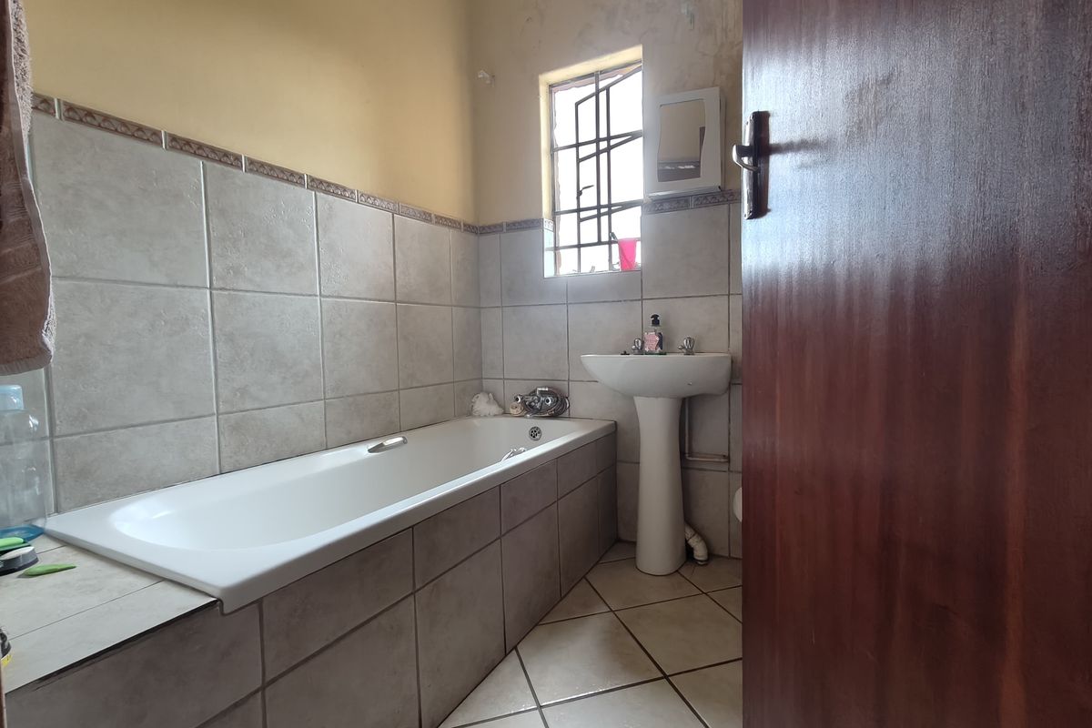 A dated bathroom featuring a built-in bathtub, pedestal basin, and tiled finishes, requiring cosmetic updates to the ceiling and wall surfaces.