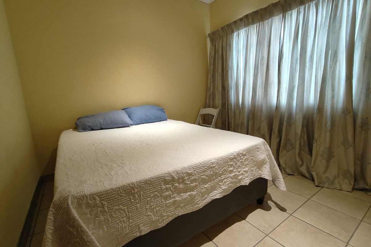 A functional bedroom featuring neutral wall tones, tiled flooring, and full-length window curtains.