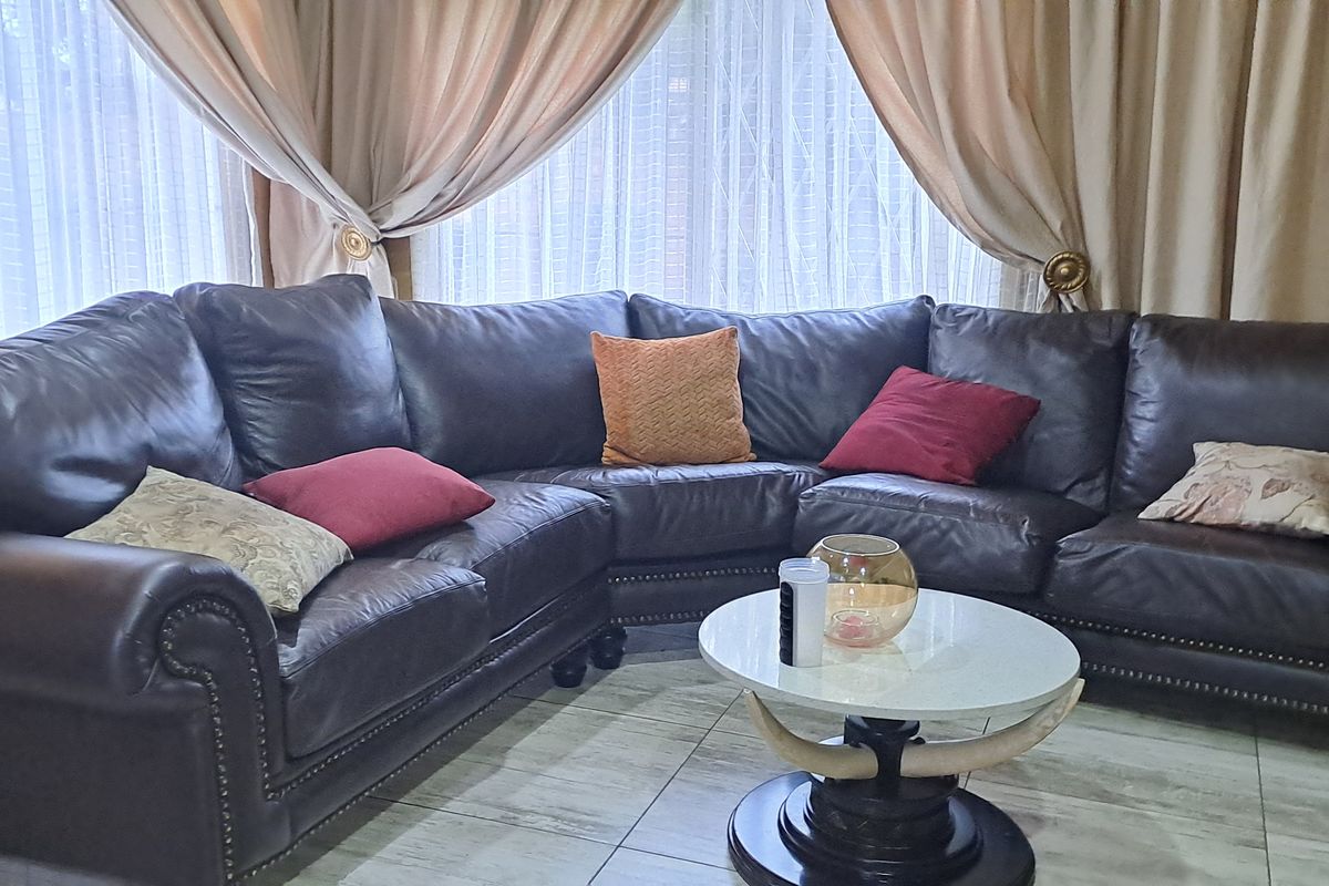 A comfortable living room area featuring tiled flooring and large windows dressed with curtains, providing a bright and inviting space.