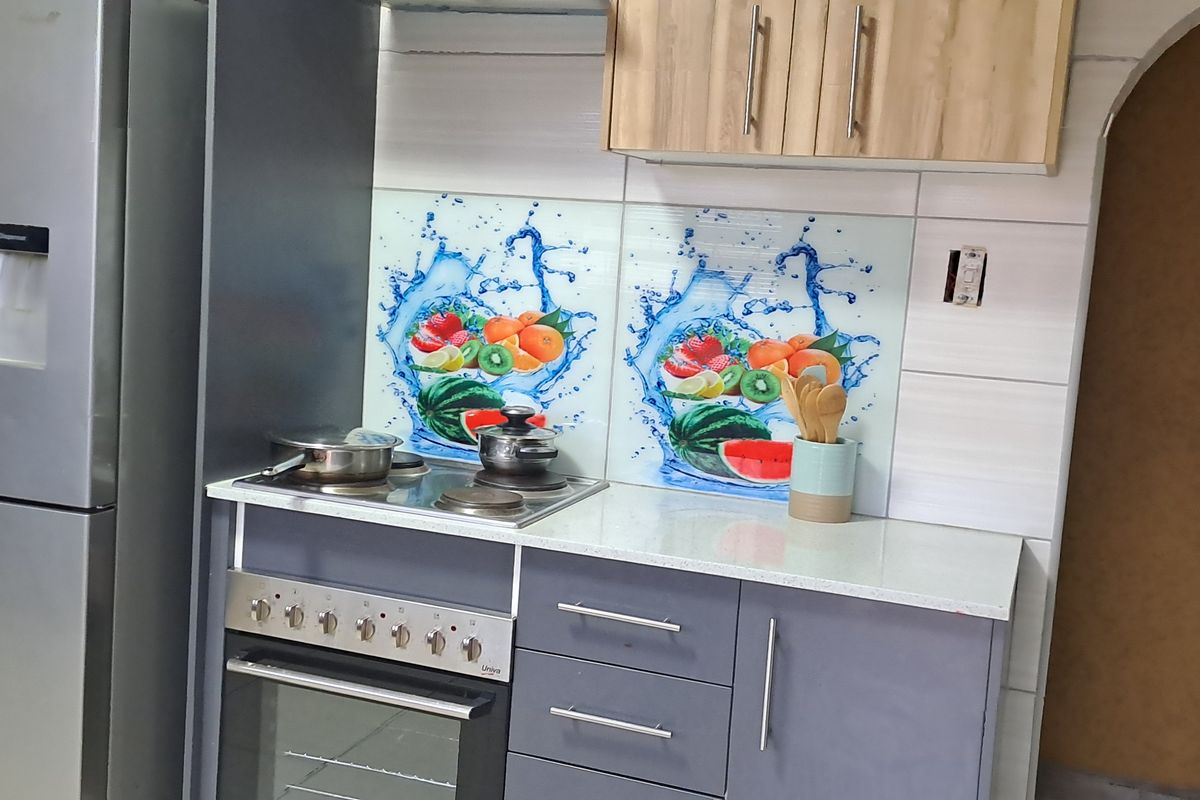A compact kitchen featuring grey cabinetry, a built-in oven with hob, and decorative fruit-themed glass splashbacks.