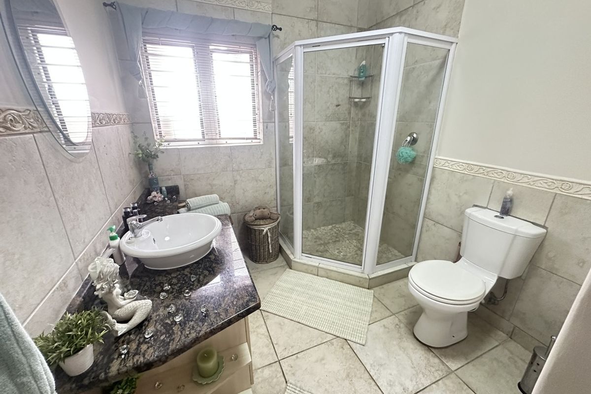 A functional bathroom featuring a corner shower enclosure, granite vanity with a vessel sink, and neutral ceramic tiling throughout.