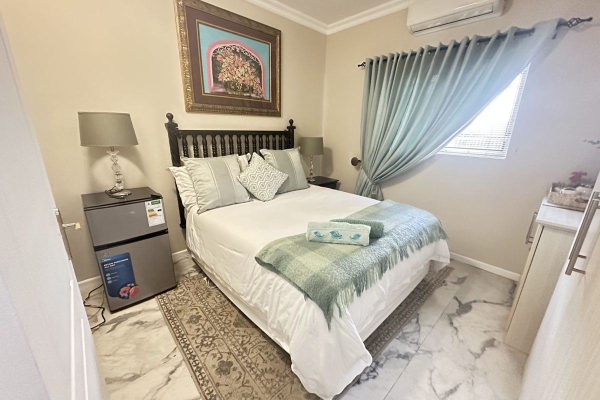 A well-maintained bedroom featuring marble-look floor tiles, decorative cornice, and a wall-mounted split-system air conditioner for climate control.