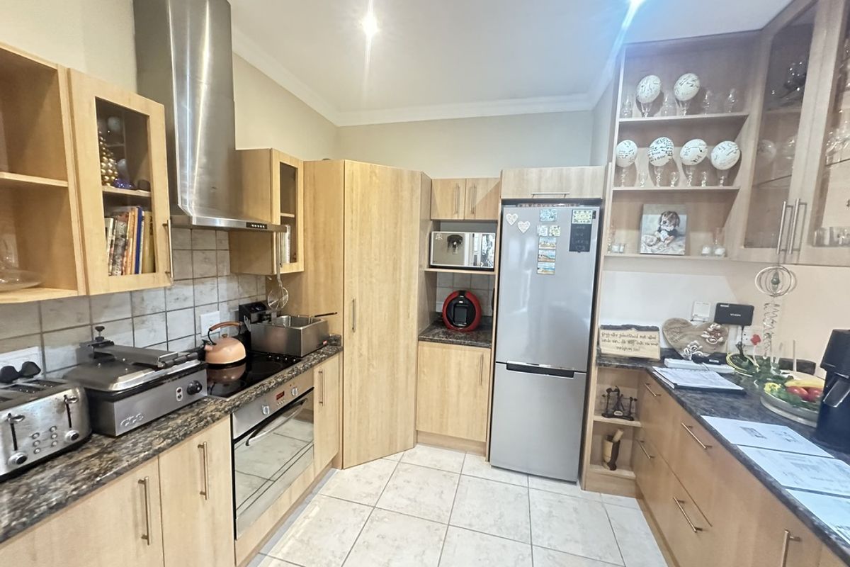 A functional kitchen featuring light wood-finish cabinetry, granite countertops, stainless steel appliances, and tiled flooring with ample storage and display shelving.