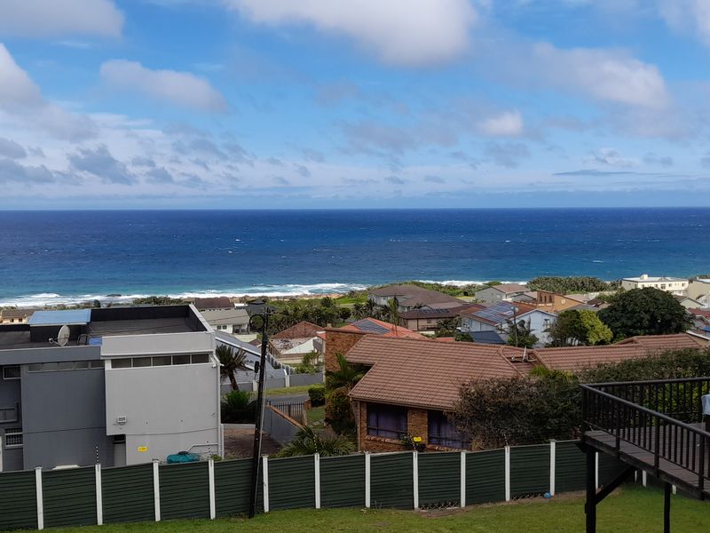 Elevated coastal view overlooking the neighborhood and ocean, featuring a wooden deck with railing and perimeter fencing.