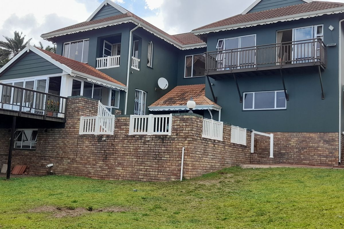 Rear view of a multi-story house featuring a raised wooden deck, brick retaining walls, upper-level balconies, and a shaded outdoor area.