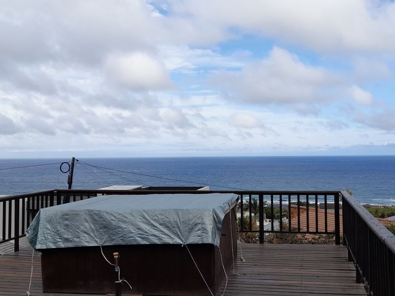 Elevated timber deck featuring a hot tub and panoramic ocean views, enclosed by a timber balustrade.