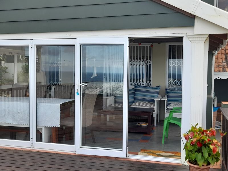 A covered patio area featuring sliding glass doors, timber decking, and tiled flooring, offering a view of the surrounding area.