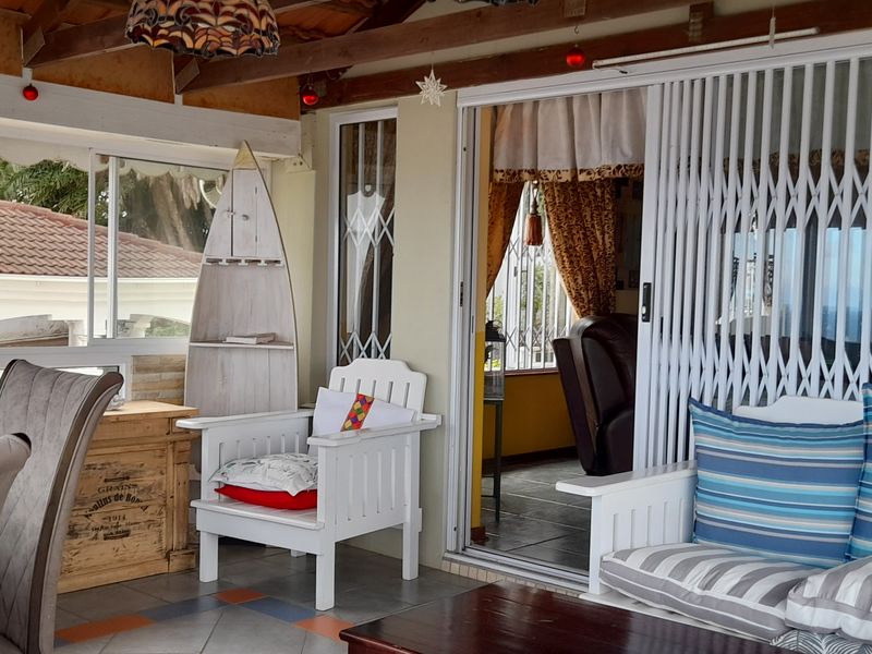 A covered patio area featuring exposed timber rafters, tiled flooring, and sliding glass doors with security gates leading into the main living space.