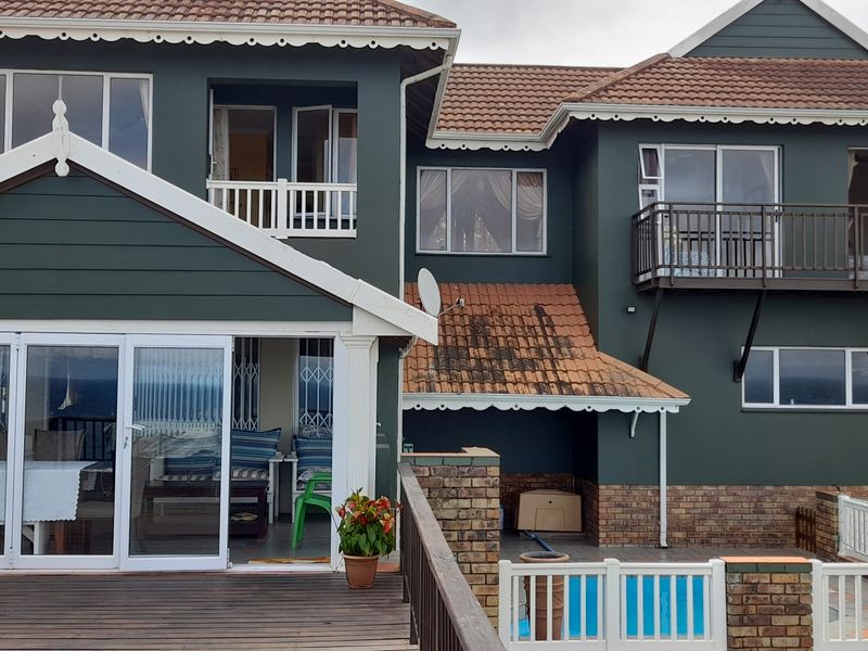 Rear elevation of a multi-story house featuring a timber deck, swimming pool, and upper-level balconies with dark exterior cladding.