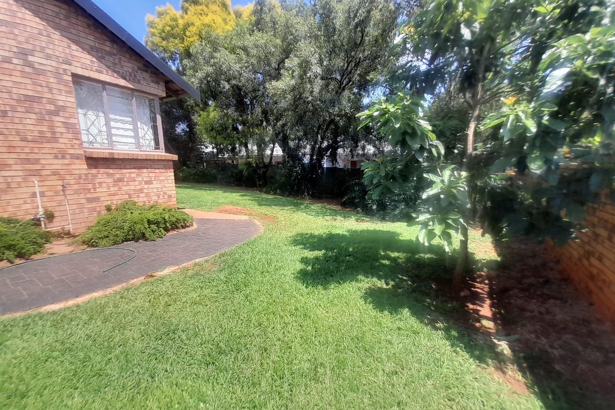 A view of the rear garden featuring a brick exterior wall, a paved walkway, and established trees and lawn.